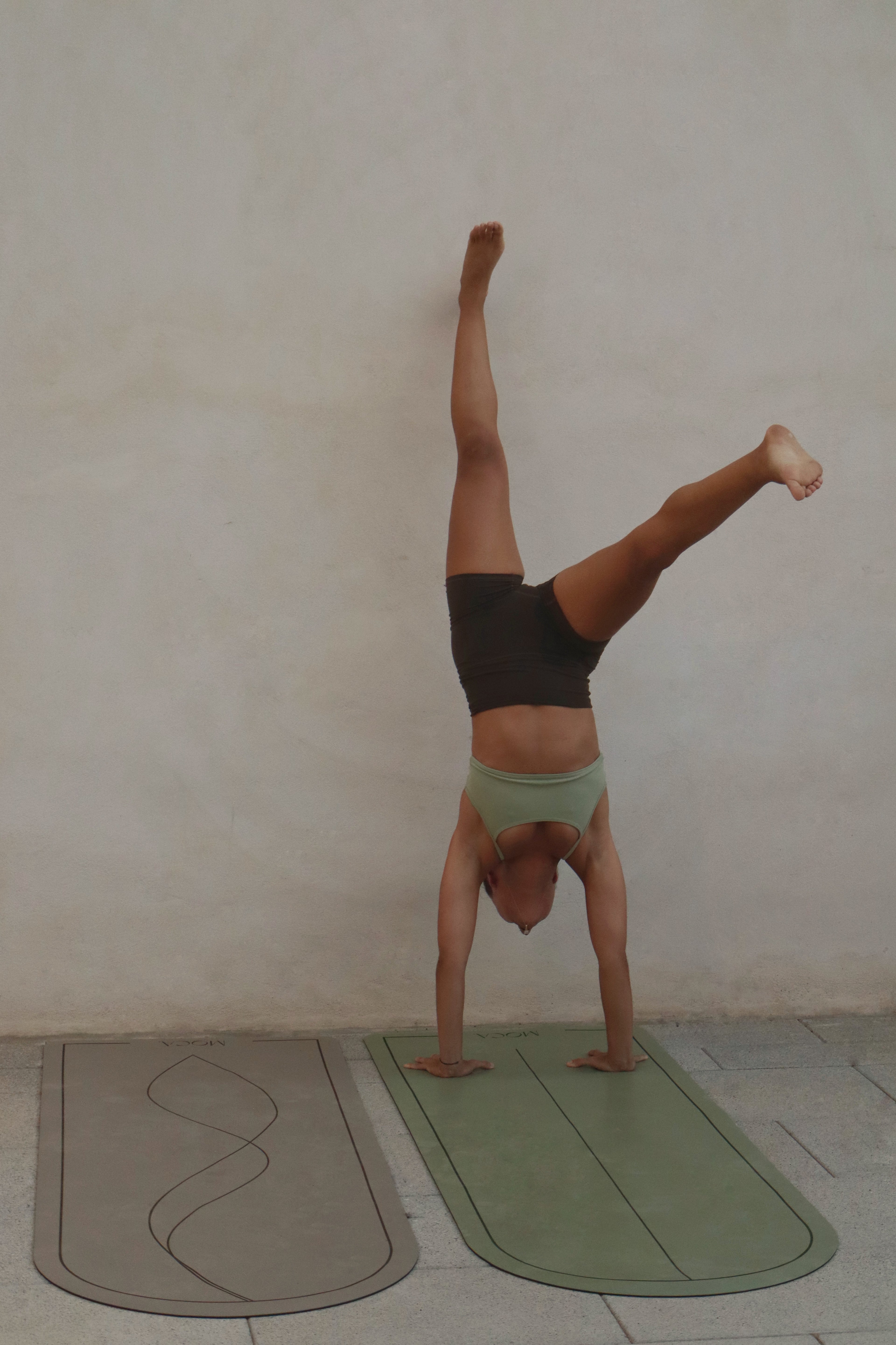 Person performing a handstand on a moca yoga mat against a plain wall.